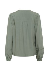 Blusa verde realizzata in tessuto morbido, con maniche lunghe, schiena plissettata e cuciture decorative lungo i polsini.
