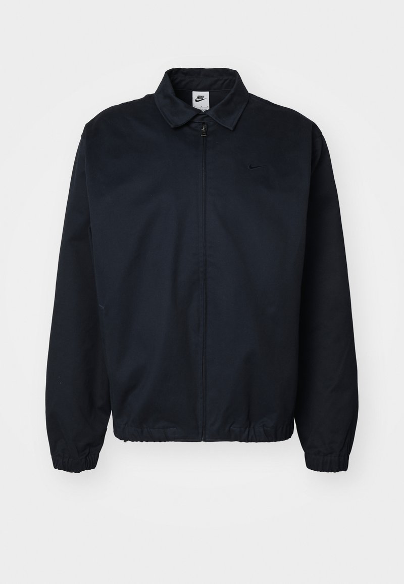 Veste Nike, bleu marine, en matière légère, avec col, fermeture éclair sur toute la longueur, poignets élastiques, design épuré avec un petit logo sur la poitrine.