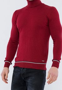 Czerwony sweter polo wykonany z miękkiego materiału, z prążkowanymi mankietami i dołem oraz kontrastowym poziomym paskiem. Dopasowany fason.