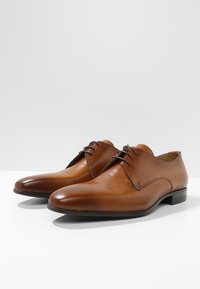 Chaussures habillées en cuir marron avec une finition lisse, un bout arrondi et un laçage, présentant des détails de couture minimaux et un talon bas en bloc.