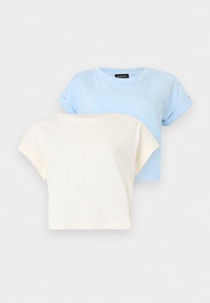 Deux t-shirts en coton à manches courtes pliés, l'un bleu clair et l'autre crème, présentés sur un fond blanc uni.