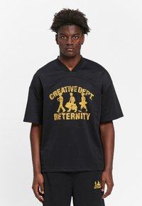 Black mesh short-sleeve jersey with V-neck, featuring gold text "CREATIVE DEPT. ETERNITY" and figures, accompanied by matching shorts.