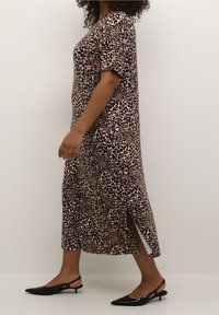 Femme marchant dans une robe midi à imprimé léopard avec manches courtes et fente latérale, portant des escarpins à talon kitten slingback noirs.