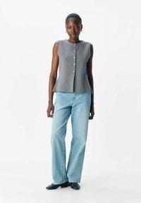 Haut sans manches gris avec un léger design peplum et cinq boutons sur le devant, associé à un jean droit bleu clair.