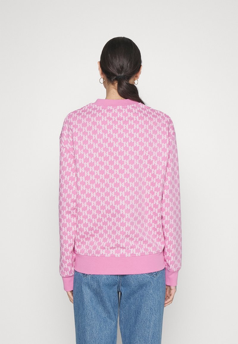 Roze sweatshirt met herhalend geometrisch patroon, geribbelde manchetten en zoom, ontspannen pasvorm, gecombineerd met blauwe spijkerbroek.