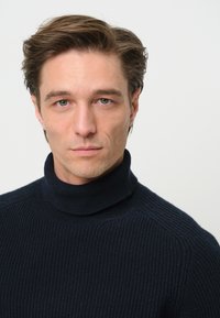 Dunkelblauer gerippter Rollkragenpullover mit eng anliegendem Kragen, strukturiertem Stoff und dezenten horizontalen Streifen, die eine strukturierte Optik erzeugen.