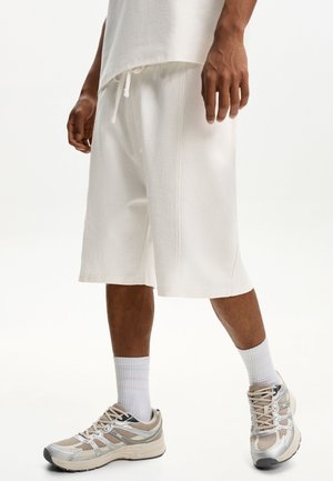 Hvide teksturerede shorts med en afslappet pasform, der har en snøre i taljen og syede detaljer. Parede med lyse grå og beige træningssko.