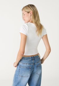Witte aansluitende t-shirt met korte mouwen, gedragen met lichtblauwe jeans met hoge taille, voorzien van twee achterzakken en rafelige randen.