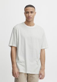White cotton t-shirt with short sleeves and a crew neck, featuring a relaxed fit and smooth texture, worn with light-colored pants.