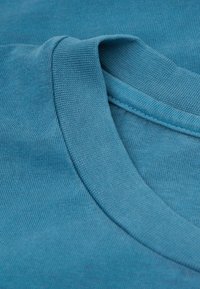 Detailní záběr na složené modré bavlněné tričko s kulatým výstřihem, které ukazuje strukturu látky a detaily šití.