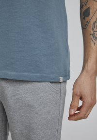 Behagelig blå bomulds t-shirt med lige kant og et lille hvidt mærke på siden, parret med lysegrå strukturerede joggingbukser.