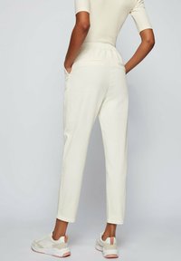 Krämfärgade joggerbyxor med avslappnad passform, elastisk midja, sidofickor och en tapered design, som är matchade med ljusa sneakers.