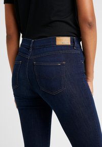 Mörkblå denimjeans med en åtsittande design, som har gula sömmar, två bakfickor och en lädermärkeslapp vid midjan.