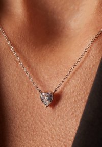 Collier en argent avec un pendentif en cristal en forme de cœur, mettant en valeur des facettes claires et une finition polie sur la texture de la peau.
