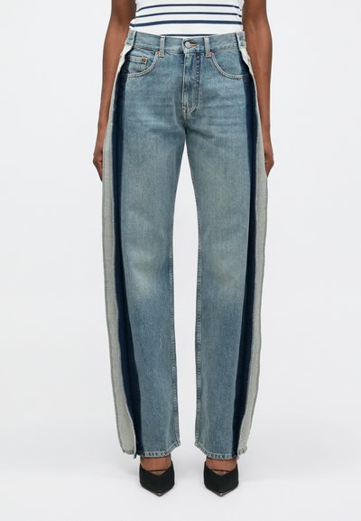 Jean large en denim avec des tons de bleu variés, présentant des panneaux latéraux contrastants, des bords bruts et un design classique à cinq poches.