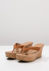 Hnědé korkové klínové sandály s texturovanými popruhy, otevřenou špičkou a tvarovanou stélkou. Mají zakřivený, pohodlný siluetu.