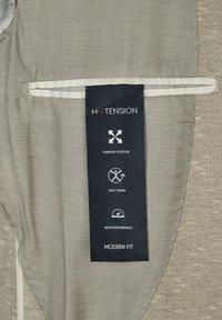 Grauer Stoff mit einem strukturierten Muster; enthält ein schwarzes Etikett mit Symbolen für Komfortstretch, einfache Anziehmöglichkeiten und hohe Leistung. Modernes Passformdesign.