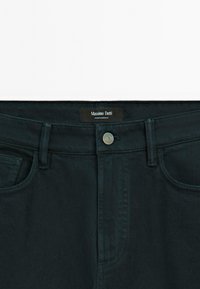 Jeans in denim nero con un bottone metallico in vita, passanti per cintura, tasche frontali e un'etichetta nera Massimo Dutti all'interno della cintura.