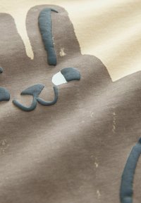 Brunt tyg visar ett kaninmönster med ljusblå accenter, inklusive stora öron, ett vitt öga och svängda linjer för morrhår, på en beige bakgrund.