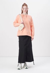 Sweatshirt pêssego com um corte solto, combinado com uma saia preta até ao tornozelo e ténis brancos. Pequena bolsa de ombro bege com detalhes em zíper.