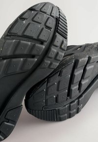 Semelles de chaussures de sport noires, avec une surface en caoutchouc texturée et un motif de semelle pour une meilleure adhérence. Les détails notables comprennent des rainures et des accents.