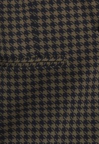 Brun och svart houndstooth-tyg med en horisontell blixtlåsficka i mitten.