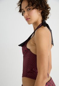 Maroon polka dot top with a halter neck and black tie detail, featuring a fitted design and textured fabric. Side view showing shape and style.