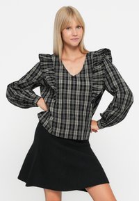 Blouse à carreaux noir et blanc avec des manches froncées et un col en V. Associée à une jupe noire évasée. Texture lisse et coupe ample.