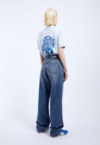Light blue short-sleeve t-shirt with a dark blue floral design on the back, paired with loose-fitting dark blue jeans and blue shoes.
