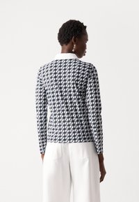 Langsleeve bovenstuk met een marineblauw en wit geometrisch patroon, voorzien van een contrasterende witte kraag en een aansluitend design. Textuurstof.
