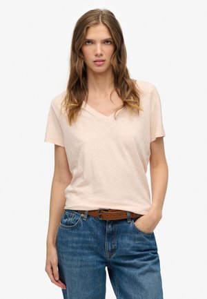 Lichtroze v-hals T-shirt gemaakt van zachte katoenen stof, met korte mouwen en een relaxte pasvorm, gecombineerd met een blauwe spijkerbroek en een bruine riem.