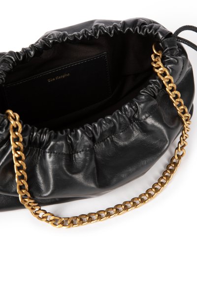 Zwarte leren tas met een samengevouwen bovenkant en een gouden kettinkje als schouderriem. Het interieur is voorzien van een donkere voering en een klein zwart vakje voor kaarten.