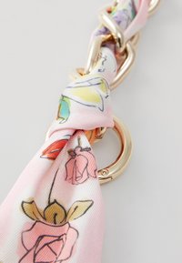 Růžový hedvábný šátek s květinovým vzorem, uvázaný kolem zlatě tónovaného kovového kroužku. Obsahuje ručně kreslené květiny v pastelových barvách. Hladký povrch.