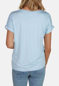 Camiseta de manga corta azul claro con puños enrollados, hecha de material suave. Presenta un ajuste holgado y un escote redondeado.