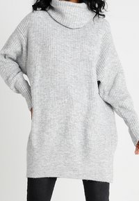 Vaaleanharmaa, ribattu neulepusero, jossa on ylisuurta, rentoa istuvuutta ja pitkät hihat. Puserossa on huomaamaton tekstuuri ja suora helma.