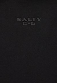 Črna majica iz blaga z značilno mat teksturo logotipa "SALTY D.G." postavljeno na sredini prsi, z ribasto teksturo.