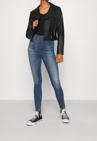 Svart läderjacka i cropped modell, ribbat svart linne, högmidjade blå skinny jeans med lätt slitage, och svarta högstövlar.