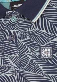 Marineblauw poloshirt met een bladenpatroon, gestructureerde stof, knoopsluiting en een prominent label met "Andes Cuyos" en het merk J&JOY.