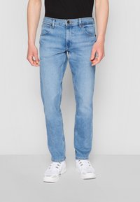 Heledad sinine teksapüksid, sirge sääre disain, viie tasku stiil, metallist nupuga kinnitussüsteem ja minimaalne kulumus. Komplementeeritud valgete tossudega.