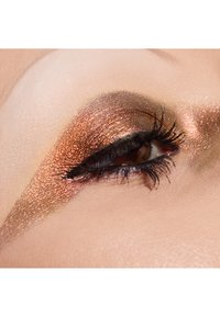 Gros plan sur un œil avec un fard à paupières en bronze pailleté, un eye-liner noir et de longs cils noirs sur un fond de peau lisse.