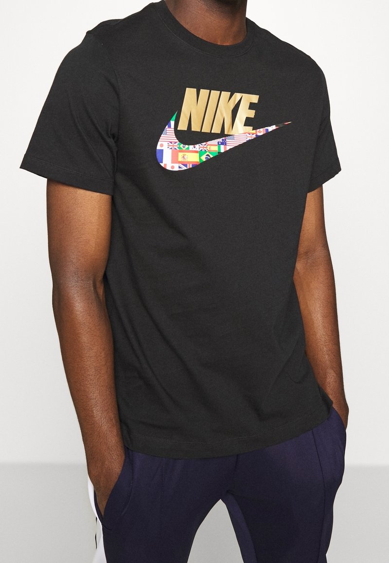 Svart t-shirt med ett guld "Nike"-logotyp, som har ett färgglatt mönster av länders flaggor inom logotypen. Korta ärmar, tillverkad av bomull.