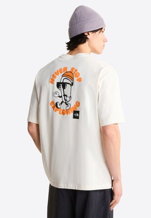 Junge Person trägt ein weißes T-Shirt mit einer orange-schwarzen Comicfigur und dem Text "Never Stop Exploring" auf der Rückseite.