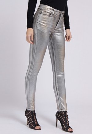 Slim-fit metalliske sølvbukser med forlommer, kombineret med sort langærmet top og sorte åbne høje hæle med gitterdesign.