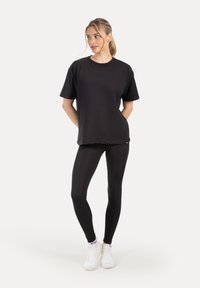 Zwart T-shirt met korte mouwen en een ronde hals, gecombineerd met zwarte leggings en witte sneakers. Soepele stof, ontspannen pasvorm, zonder zichtbare patronen.