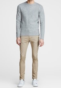 Suéter gris de punto con dobladillo acanalado, combinado con chinos beige de corte slim y zapatillas blancas de caña baja. Líneas limpias y texturas sutiles.