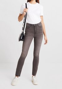 Jeans ajustados grises de cintura alta, combinados con una camiseta blanca y zapatillas blancas. Se lleva una pequeña bolsa negra al hombro.