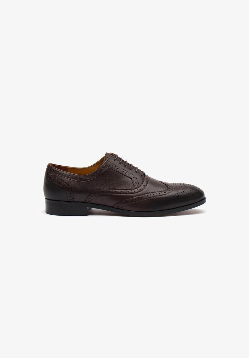 Scarpa da uomo in pelle marrone con design wingtip, dettagli brogue, punta tondeggiante e tacco basso nero. Texture liscia e forma classica.