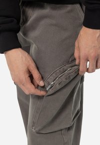 Cargo pants in dark gray fabric with a textured surface, featuring a side zipper pocket and tapered leg design.