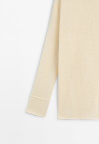Long sleeve of a soft, cream-colored knitted sweater with a wide cuff detail on a plain white background.