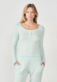 Długi rękaw, mięta zielona bluzka o prążkowanej fakturze, okrągły dekolt i zapięcie na trzy guziki; połączona z dopasowanymi, wąskimi spodniami.